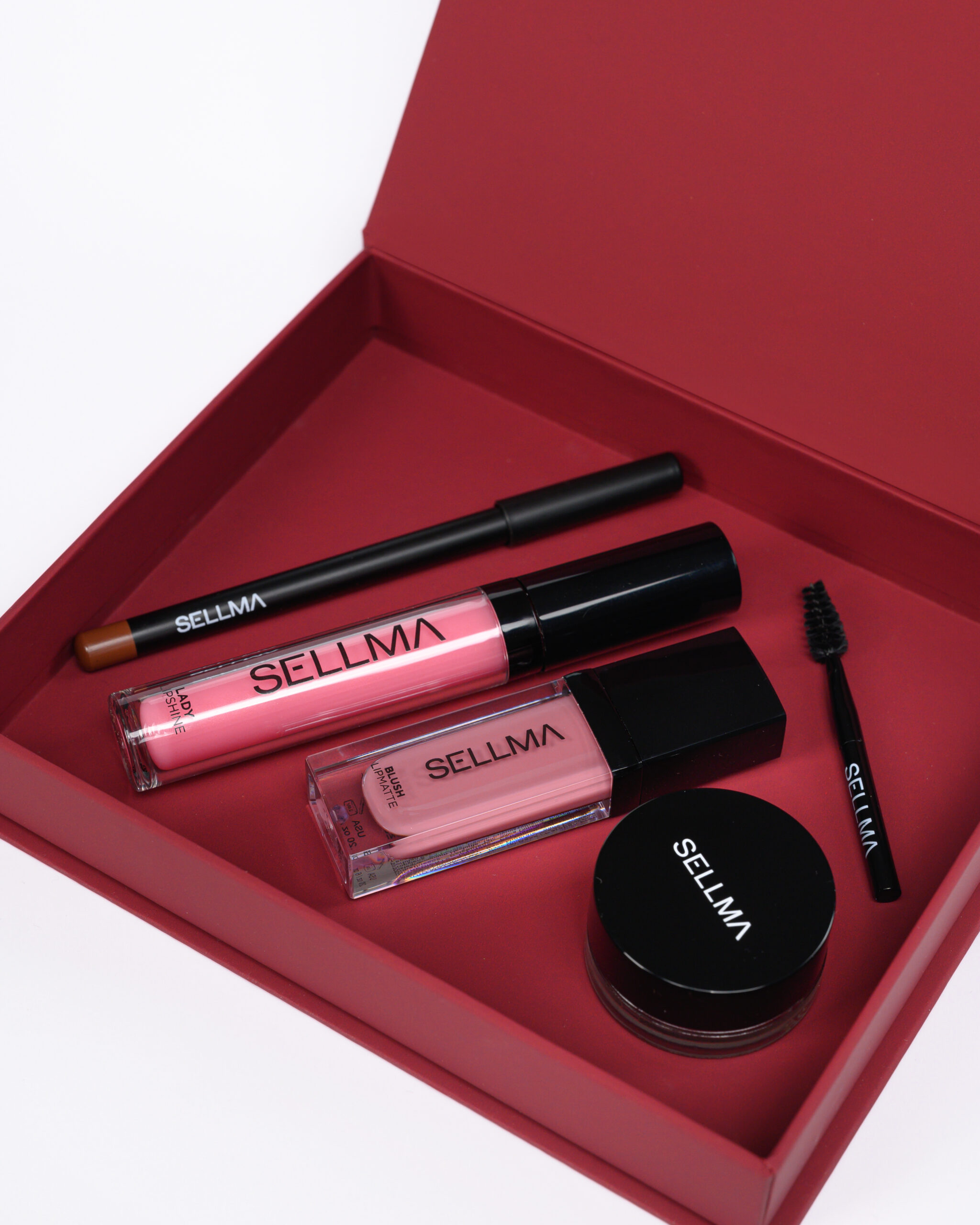 Red lipstick and lip gloss set in an open pink box with several gloss tubes labeled SELLMA and a mascara wand visible in the corner